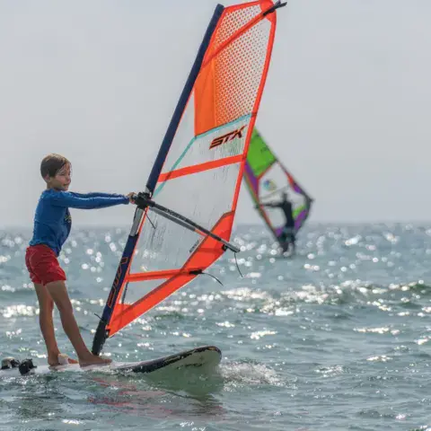 Enfant sur une planche à voile, voile orange