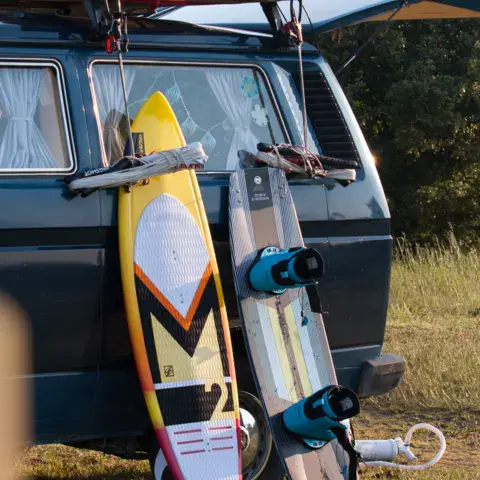 Deux planches de kite appuyées contre un combi Volkswagen