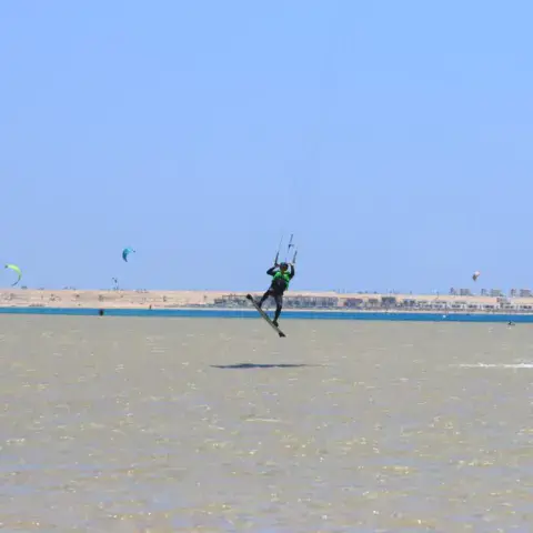 Kitesurfeur en l'air au-dessus de l'eau, plusieurs kites dans le ciel