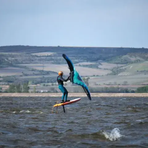 Pratiquant de wing foil sur un plan d'eau, collines à l'arrière-plan