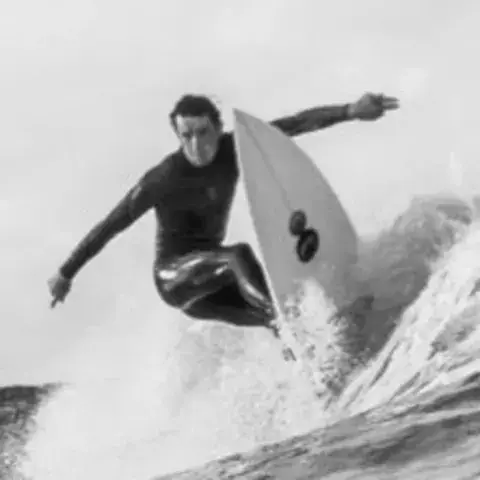 Surfeur en noir et blanc sur une vague, près des rochers