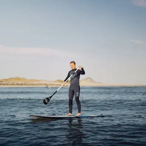 Pagayeur debout sur un stand up paddle, dunes au fond