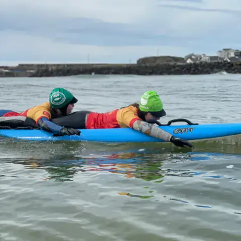 Deux personnes allongées sur une planche de surf bleue