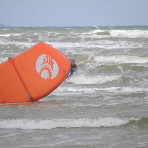 Aile de kite orange posée sur l'eau, dans les vagues