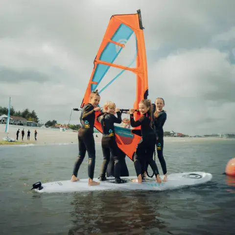 Groupe d'enfants sur une planche de windsurf, phare de Hörnum en arrière-plan