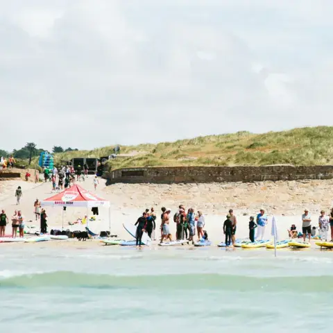 Groupe de surfeurs rassemblé sur la plage devant les dunes
