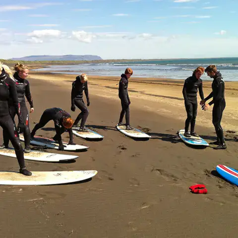 Groupe en combinaison avec des planches sur une plage de sable sombre