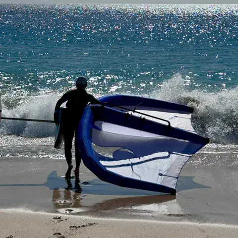 Pratiquant portant une aile de wing foil sur la plage