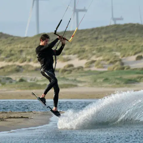 Kitesurfeur sur une eau plate bordée de dunes