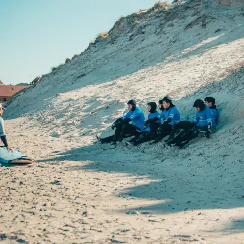 Explications d'un moniteur à des élèves assis sur une dune