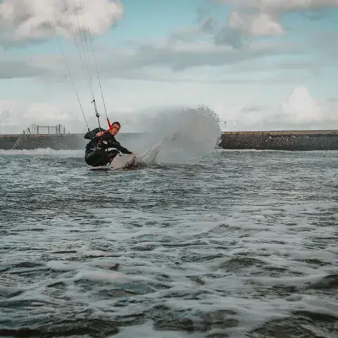 Kitesurfeur lançant une gerbe d'eau près d'une digue