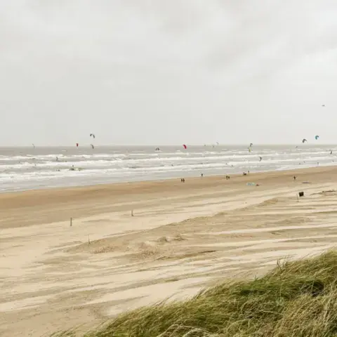 Longue plage de sable avec des kites au large