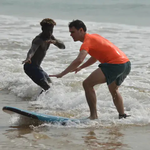 Un moniteur aide un élève à se lancer sur la vague