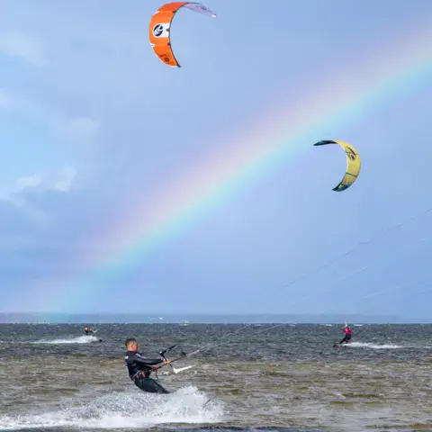 Des kitesurfeurs sous un arc-en-ciel