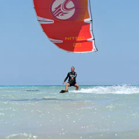 Un rider sous une aile de kite rouge, près du rivage