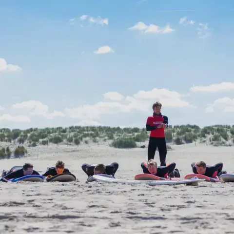 Cours de surf à terre sur la plage, élèves allongés sur leurs planches