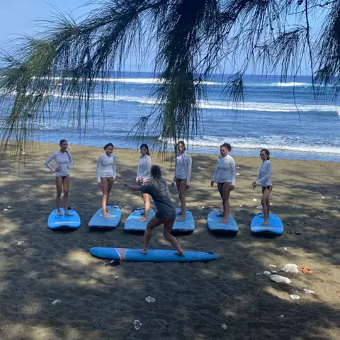 Groupe d'élèves sur leurs planches, consignes du moniteur sur la plage