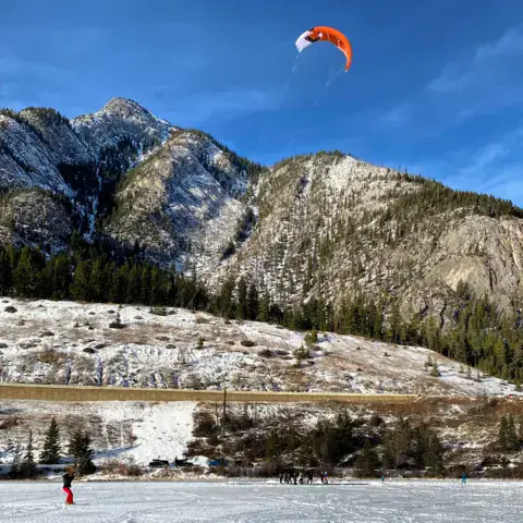 Aile de snowkite orange au-dessus d'une étendue gelée, en montagne