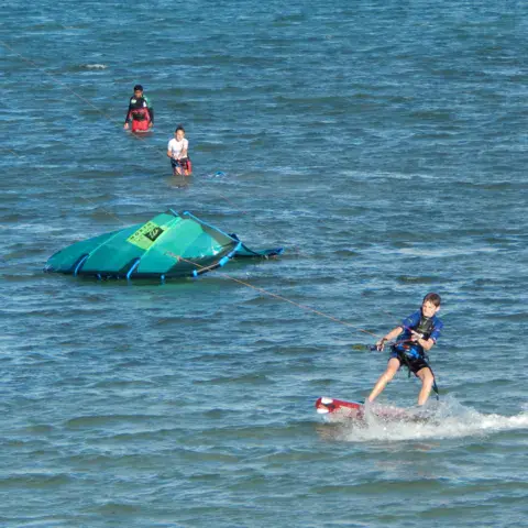 Un élève en kitesurf, son aile posée sur l'eau derrière lui