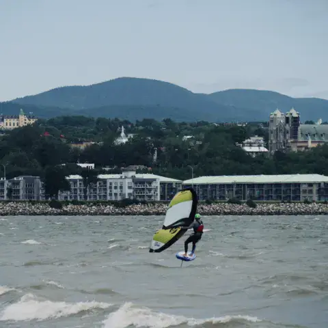 Pratiquant de wingfoil en vol au-dessus de l'eau, avec la rive en arrière-plan