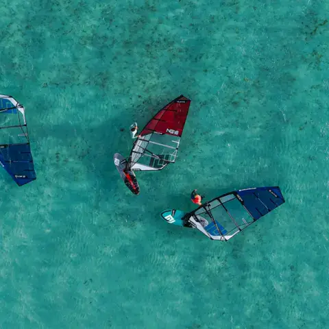 Trois windsurfeurs sur l'eau turquoise, vue du ciel