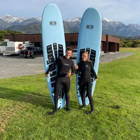 Deux surfeurs avec leurs planches sur l'herbe, face aux montagnes