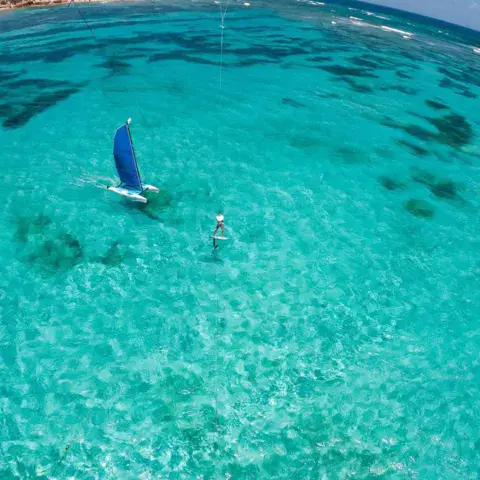 Petit voilier à voile bleue sur un lagon turquoise, vue aérienne