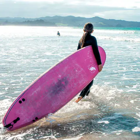 Surfeuse avec une planche rose au bord de l'eau