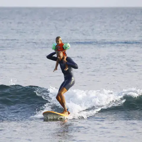 Surfeur sur une vague avec un enfant sur les épaules