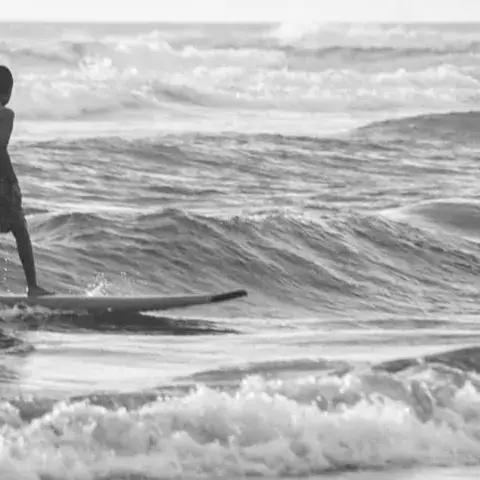 Surfeur debout sur sa planche dans les vagues, en noir et blanc