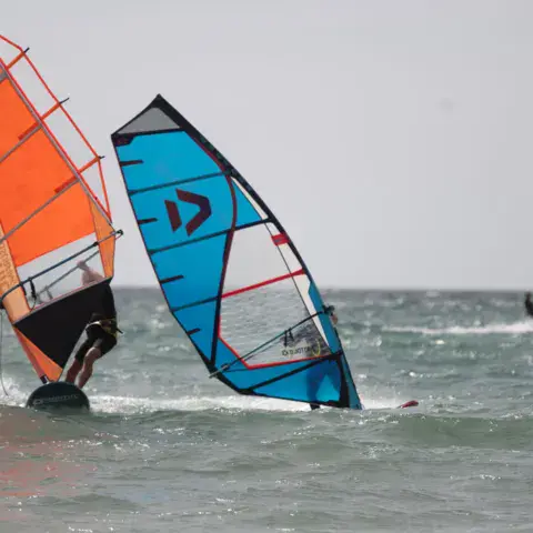 Deux planches à voile à l'eau, voiles orange et bleue