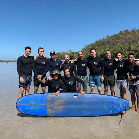 Groupe de surfeurs posant autour d'une planche bleue sur la plage