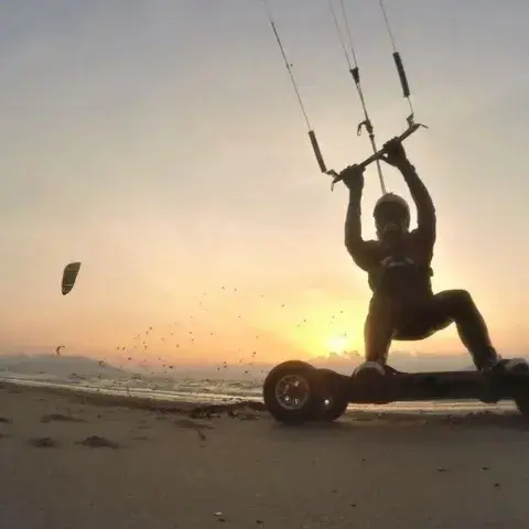 Pilote de landboard tracté par un kite au coucher du soleil