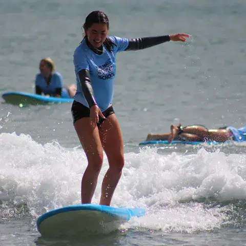 Élève debout sur sa planche dans les vagues, moniteur derrière