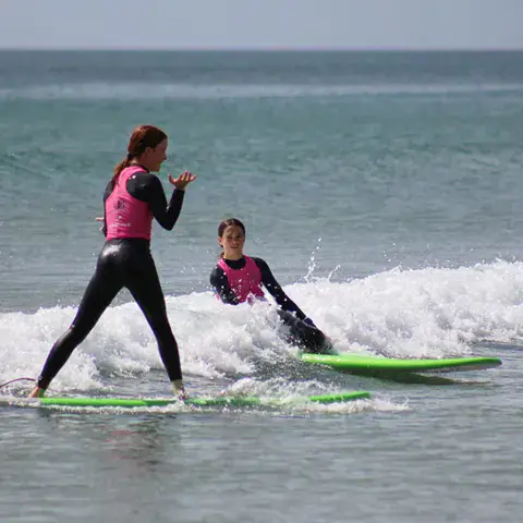Deux surfeuses dans les vagues, l'une debout sur sa planche verte