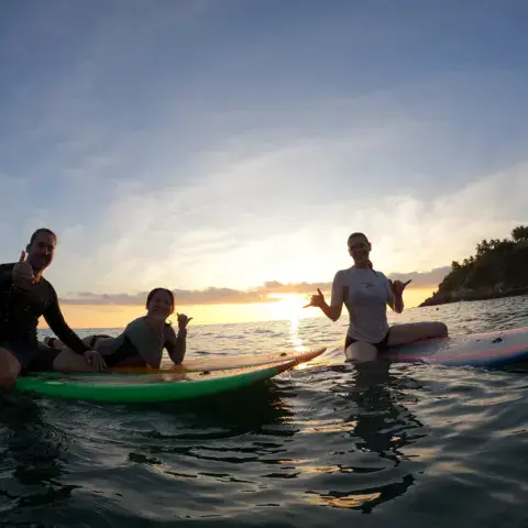 Groupe assis sur des planches dans l'eau au coucher du soleil