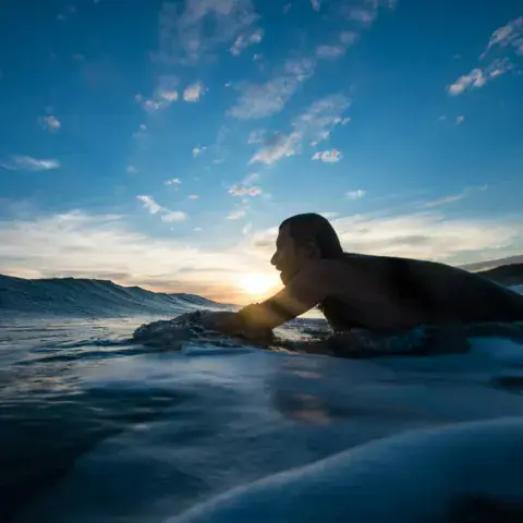 Surfeur allongé sur sa planche, soleil bas sur l'eau