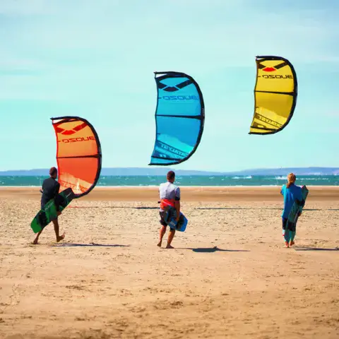 Trois kitesurfeurs avec leurs ailes sur la plage