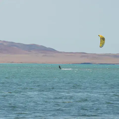 Kitesurfeur sur l'eau turquoise de la baie, dunes du désert en arrière-plan
