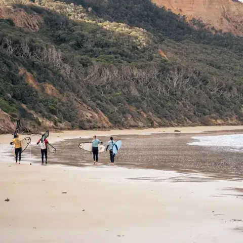 Des surfeurs marchent sur une plage au pied de falaises