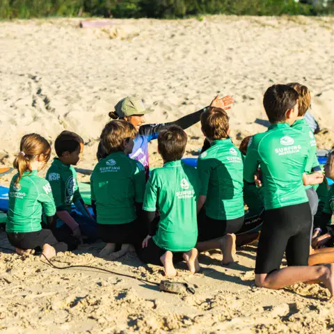 Groupe d'enfants en haut vert sur la plage avec un moniteur