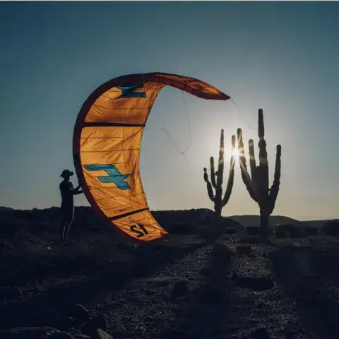 Kite gonflé au coucher du soleil, entre des cactus
