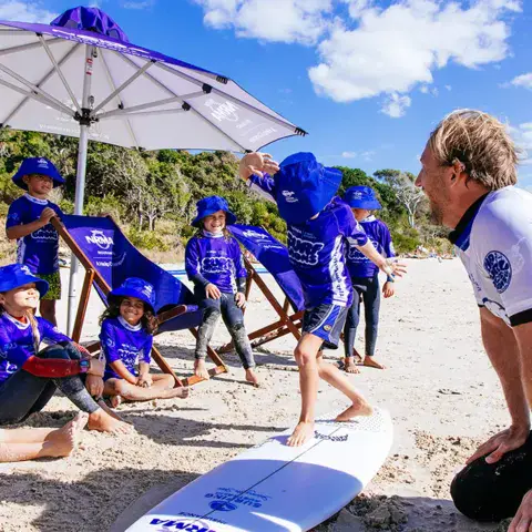 Moniteurs et groupe d'enfants sur la plage, sous un parasol