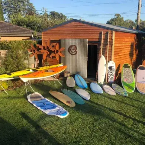 Planches, paddles et kayaks alignés sur la pelouse devant l'abri de jardin