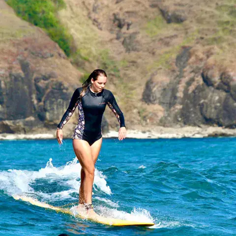 Surfeuse sur une vague devant la côte rocheuse