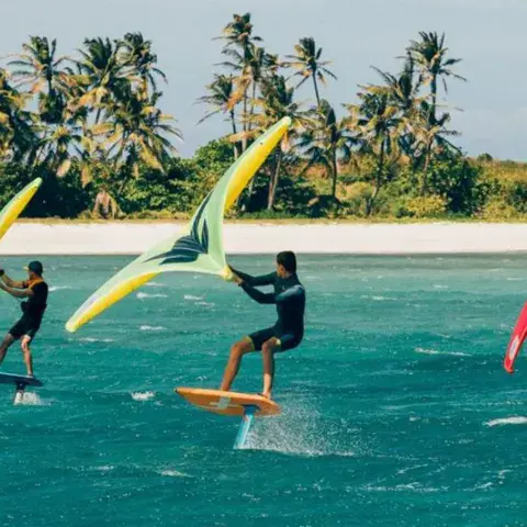 Trois pratiquants de wing foil sur une eau turquoise