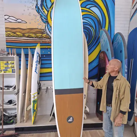 Longboard bleu clair et marron dans la boutique, planches rangées au fond