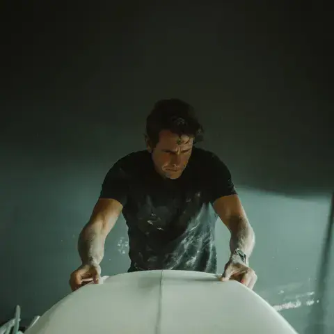 Façonneur penché sur une planche de surf dans l'atelier