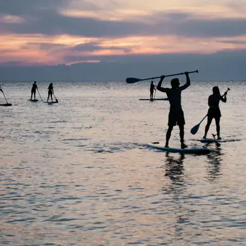 Pratiquants de stand up paddle sur l'eau calme au coucher du soleil