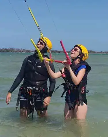 Deux élèves casqués apprenant à piloter l'aile, dans l'eau peu profonde